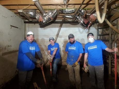 team members in a water damaged basement, holding tools and wearing hats, masks and blue Operation Blessing t-shirts