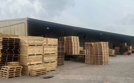 several stacks of high-quality pallets at Pasadena Skid & Pallet outdoors near a large outbuilding